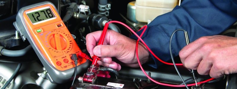 An auto mechanic uses a multimeter voltmeter to check the voltage level in a car battery.
